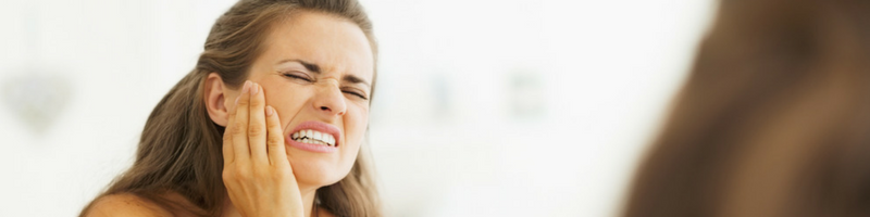 A young woman grimaces in dental pain due to an unknown cause.