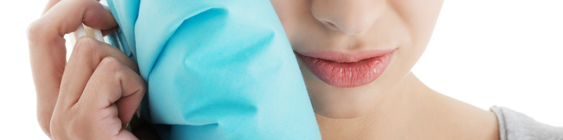 A young woman holds a cold compress to her jaw in order to alleviate root canal pain.
