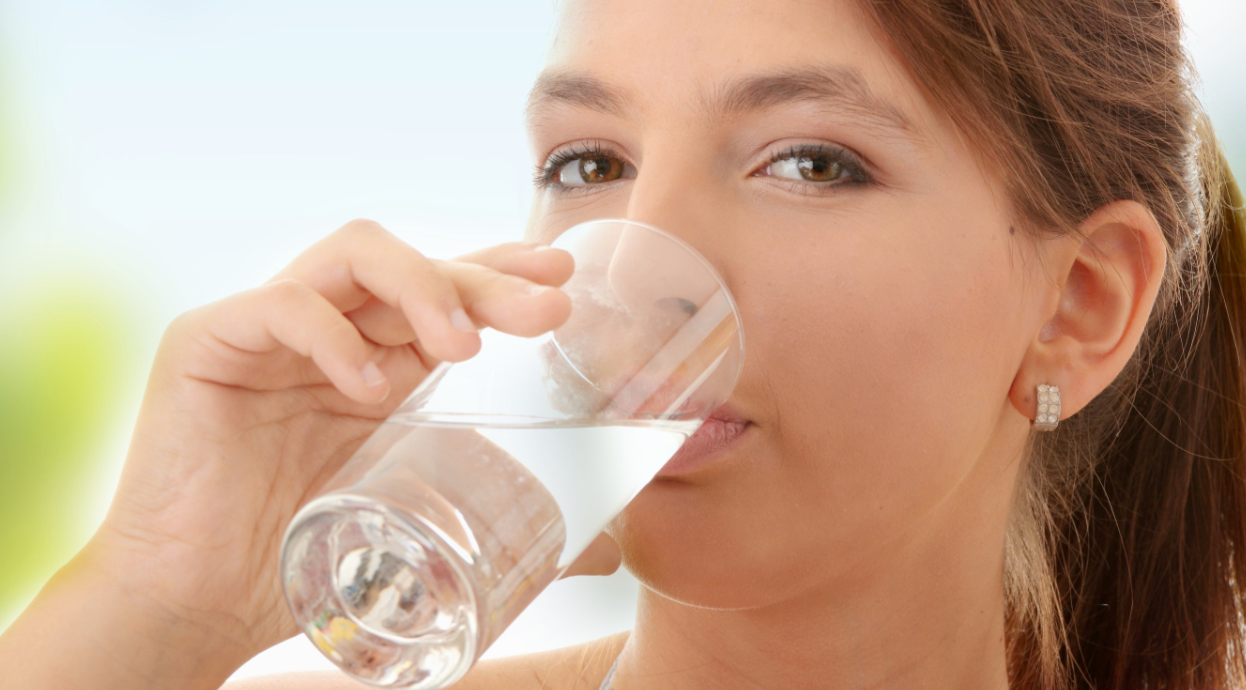 A young woman drinks water for healthier teeth.